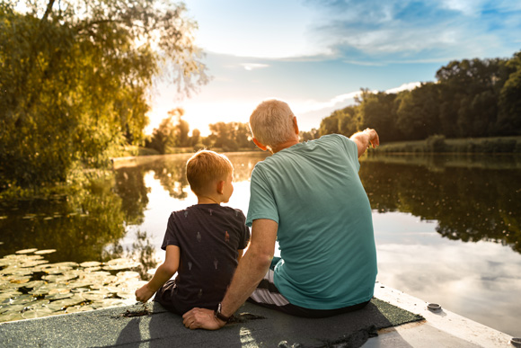 kid and grandfather sitting by a lake