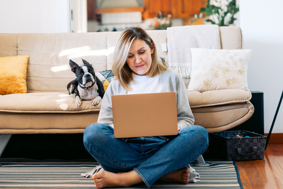 woman sitting on floor with laptop, dog on sofa behind