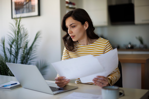 woman sitting at a laptop holding papers